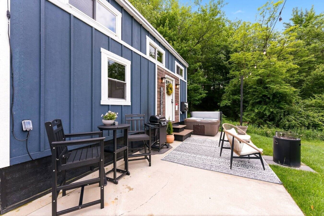 Een blauw huis met een patio, voorzien van buitenmeubilair, een jacuzzi en een barbecue.
