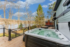 A hot tub on a wooden deck with a view of a lake and trees. - Lakefront! Sauna! HotTub! Sleeps 14! 1.5M to Wisp! (McHenry)