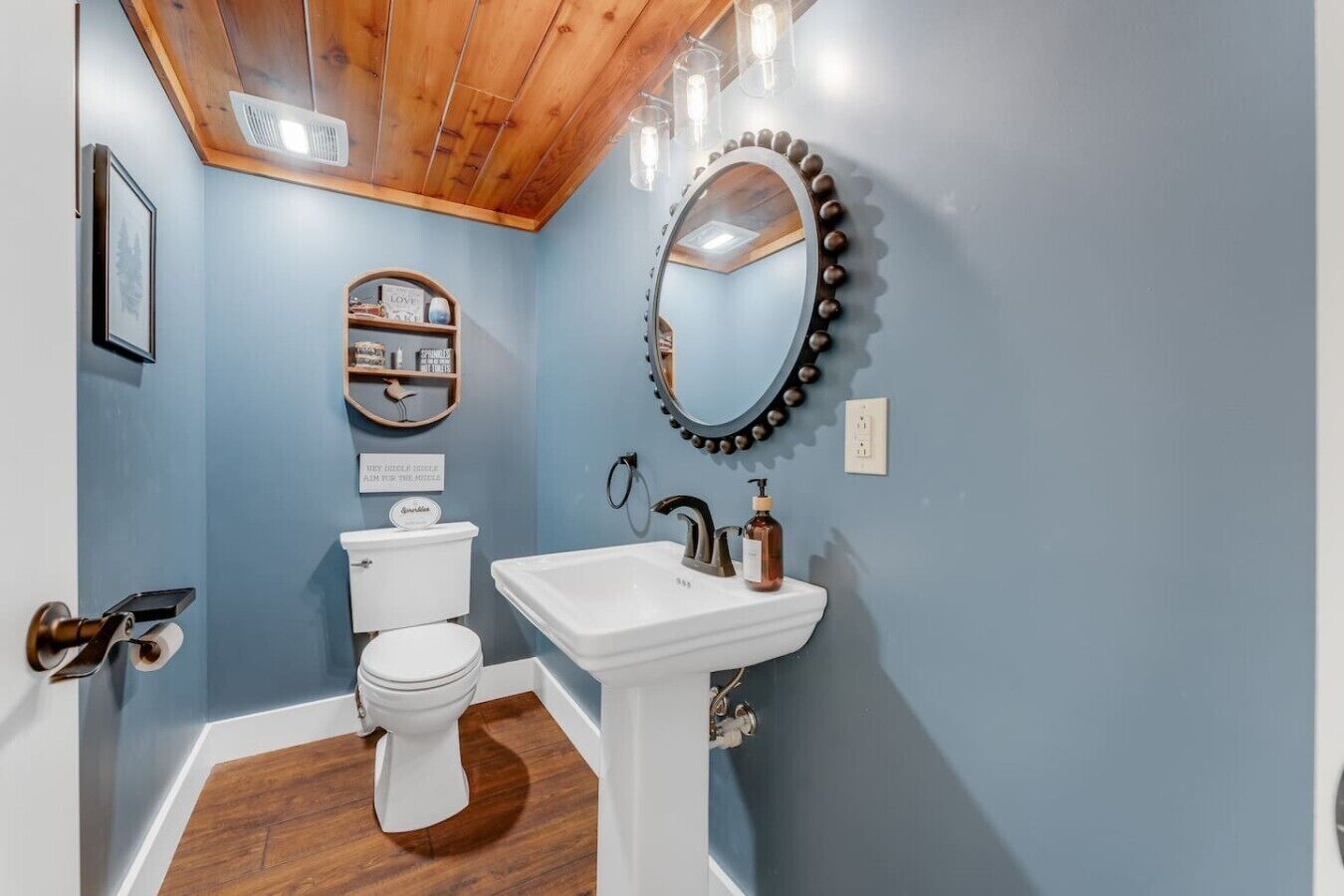 A bathroom with a toilet, sink, vanity mirror, and wooden ceiling.
