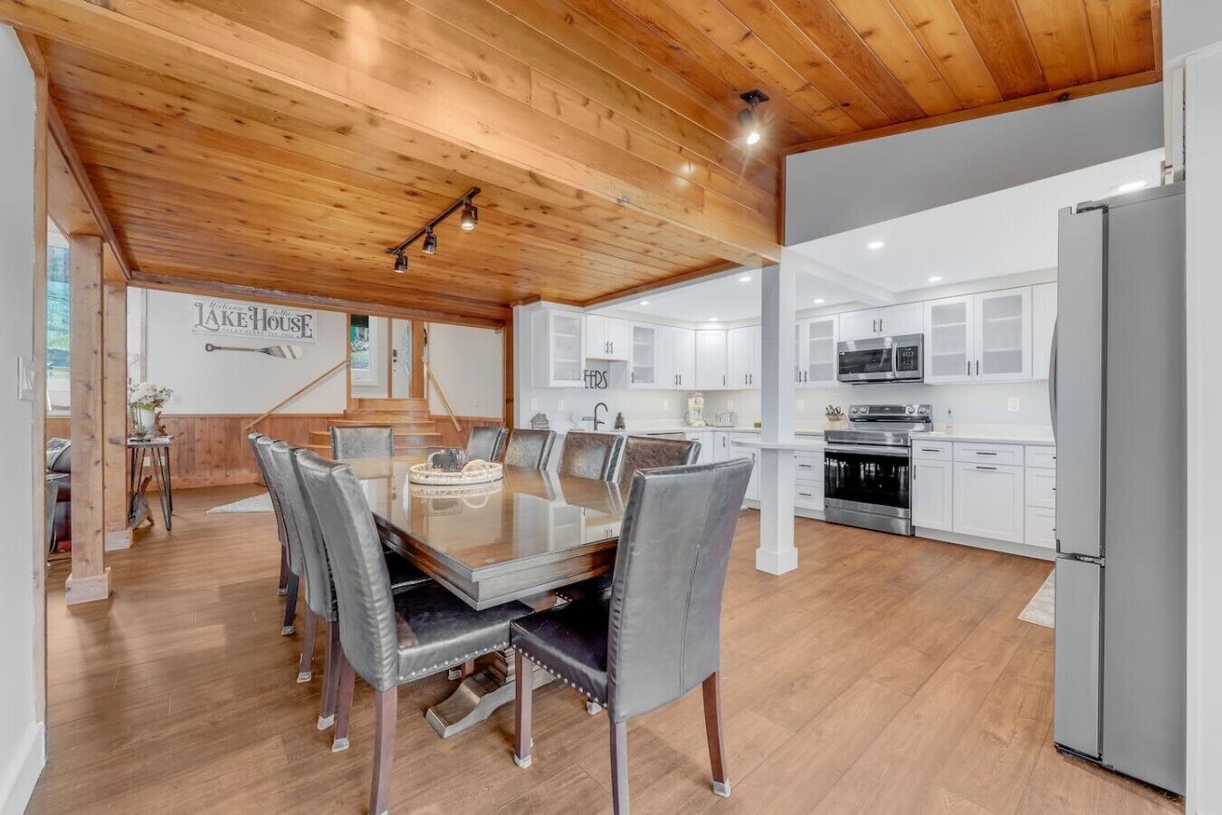 A modern kitchen with white cabinets, stainless steel appliances, and a wooden ceiling.