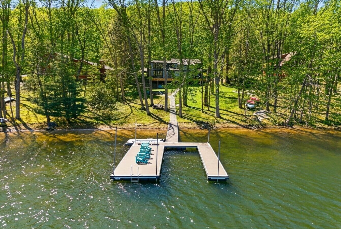 A lakeside dock with a boat, surrounded by trees and a building in the background.