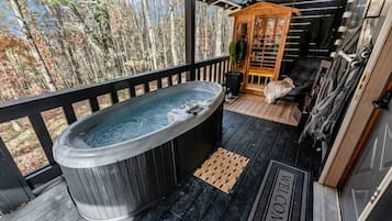 Un jacuzzi en una terraza de madera con vistas a árboles, una estructura de madera y una puerta que dice 'WELCOME'.