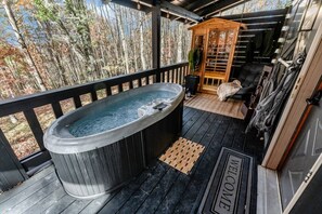 Un jacuzzi en una terraza de madera con vistas a árboles, una estructura de madera y una puerta que dice 'WELCOME'.
