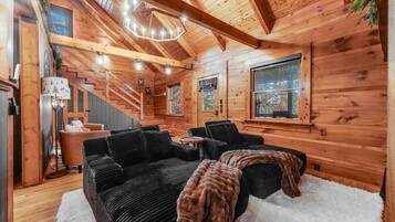 Interior acolhedor de uma cabana com escada, um sofá preto e um candelabro.