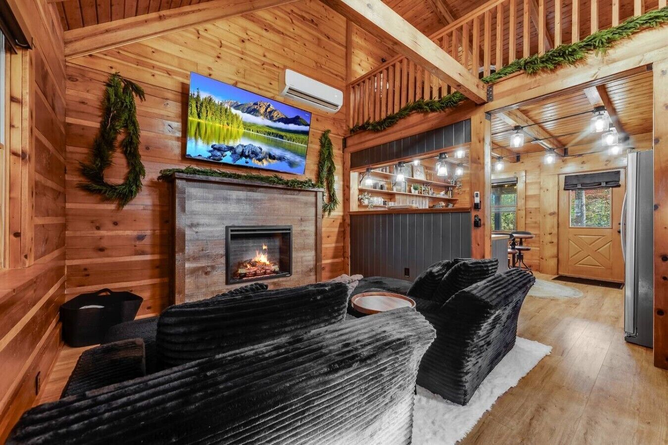 Interior acolhedor de uma cabana com lareira, uma televisão montada acima e uma área de estar com tapete.
