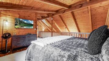 Quarto de cabana de madeira com cama, penteadeira e uma pintura de paisagem montanhosa.