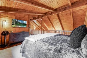 A wooden cabin bedroom with a bed, dresser, and a painting of a mountain landscape.