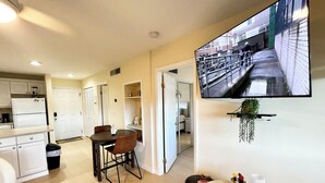 A modern apartment with a kitchen, dining area, and a living room with a TV mounted on the wall. - OV 123 Tennis Court View - Welcome To Paradise! (Fort Pierce)