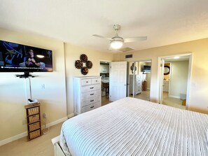 Ein Schlafzimmer mit Bett, Kommode, Fernseher und Deckenventilator.