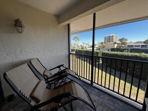 Ein Balkon mit gepolstertem Stuhl, einer Wandleuchte und Blick auf ein Wohngebiet mit Gebäuden und Grünflächen.