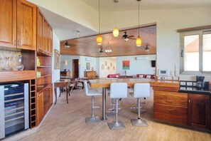 Eine Küche mit Holzausstattung, einer zentralen Kochinsel mit Barhocker, Pendelleuchten und einem Deckenventilator.