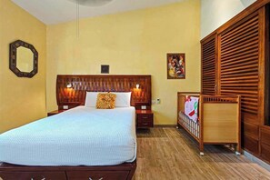 Ein Hotelzimmer mit einem großen Bett, einem Holzkopfteil, Nachttischen, einem Beistelltisch, einem Babybett und einem Kleiderschrank.