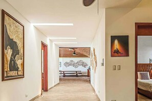 Ein Flur mit Kunstwerken an den Wänden, einer hölzernen Bank und einem Deckenventilator.