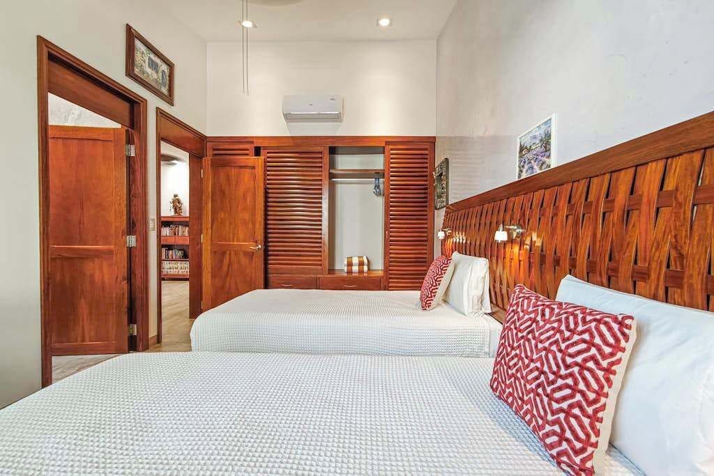 A bedroom with two beds, wooden headboard, a wardrobe, and a mirror.