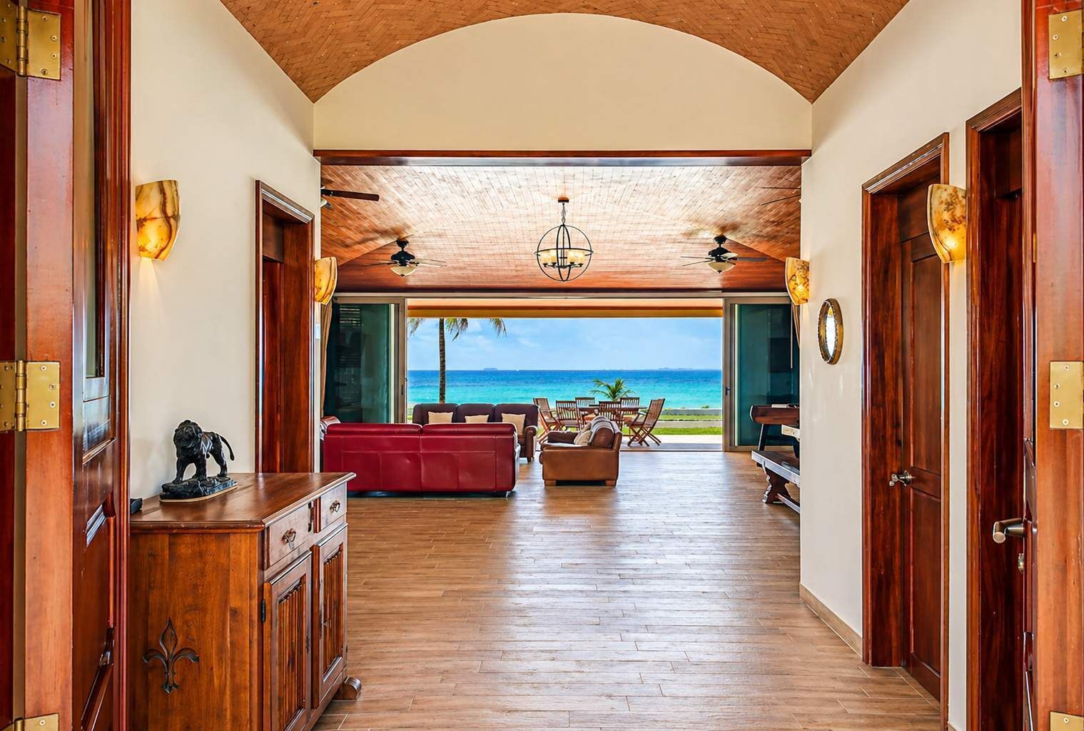 A spacious hallway with wooden floors and walls, leading to a seating area with a view of the ocean.