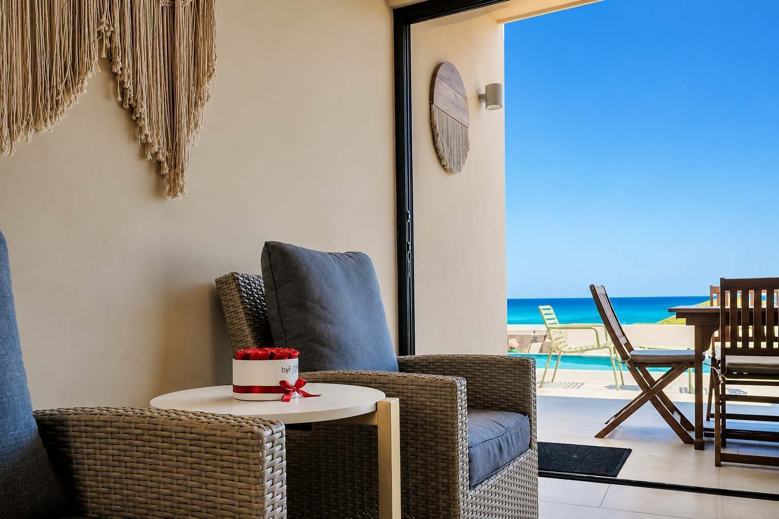 A balcony with wicker furniture, a small table with a cake, and a view of the ocean.