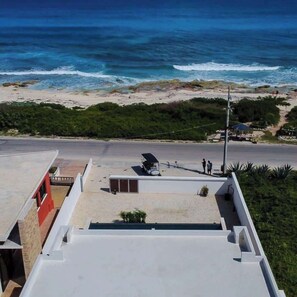 A rooftop with a view of the ocean, a small building, and a road with a few people. - Villa Sol | 2BR Ocean View & Pool | Isla Mujeres (Isla Mujeres)