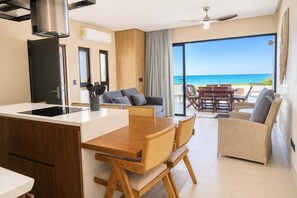 A modern kitchen with a central island, a dining area with wooden furniture, and a balcony with a view of the ocean. - Villa Sol | 2BR Ocean View & Pool | Isla Mujeres (Isla Mujeres)