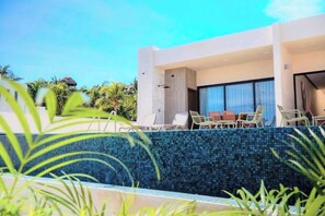 A modern building with a pool, lounge chairs, and a view of palm trees. - Villa Sol | 2BR Ocean View & Pool | Isla Mujeres (Isla Mujeres)