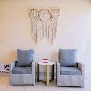 A room with two grey wicker armchairs, a small round table with a red object, and a macramé wall hanging. - Villa Sol | 2BR Ocean View & Pool | Isla Mujeres (Isla Mujeres)