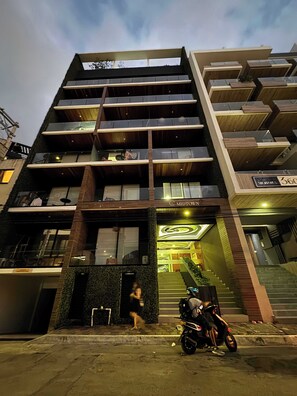 Ein mehrgeschossiges Gebäude mit moderner Architektur, das Balkone, große Fenster und einen markanten Eingang mit einer Treppe aufweist.