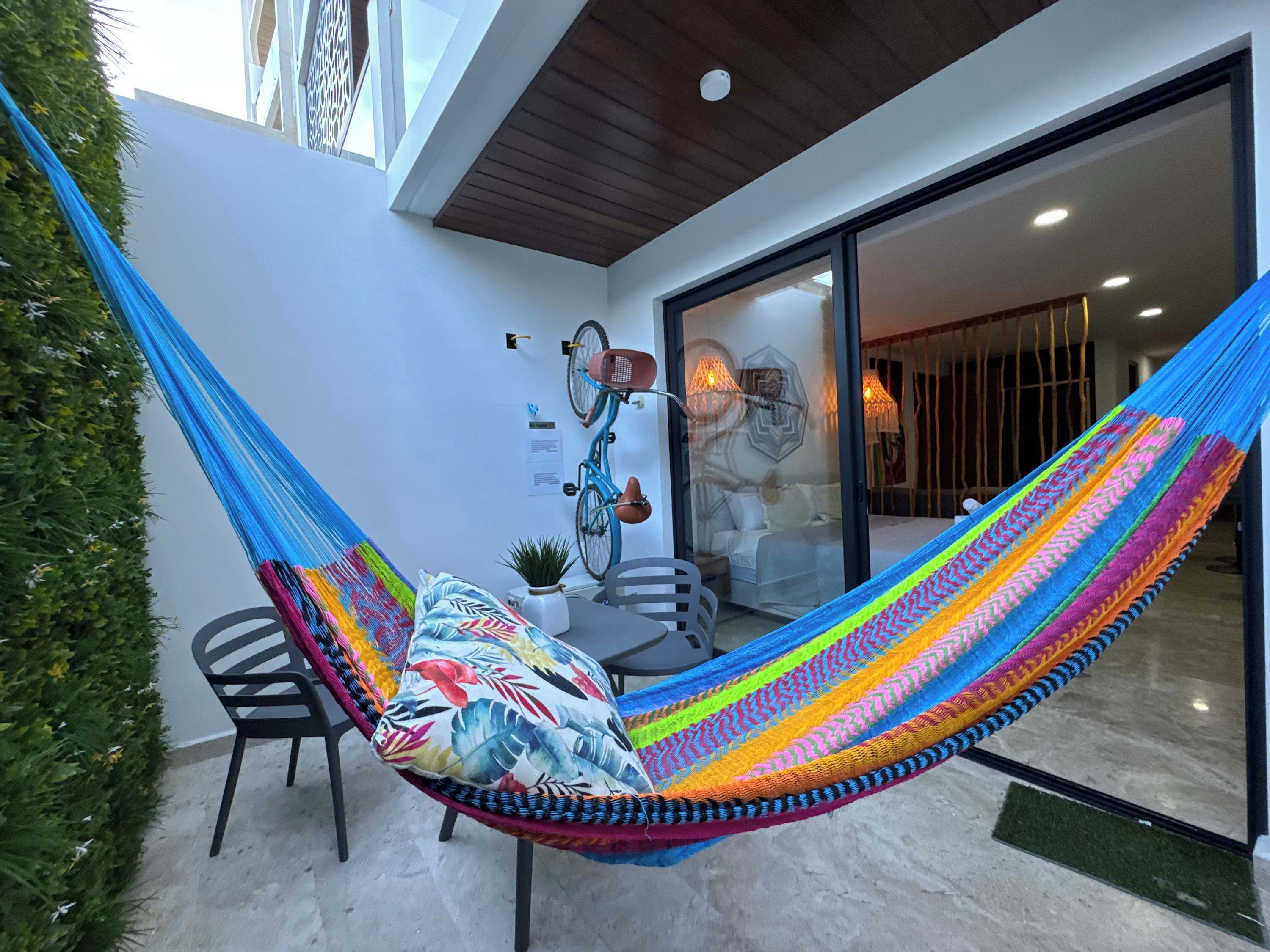 A hammock chair with a colorful hammock, a bicycle, and a potted plant in a modern outdoor space.