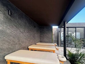 A modern spa area with three massage tables, a stone wall, and a glass door leading to an outdoor space. - Chic Studio · Rooftop Pool · 1 Blk to 5th Ave (Playa del Carmen)