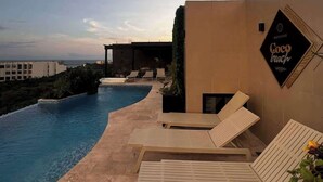 A poolside area with lounge chairs, a sign reading 'Coco Beach,' and a view of the ocean. - Chic Studio · Rooftop Pool · 1 Blk to 5th Ave (Playa del Carmen)