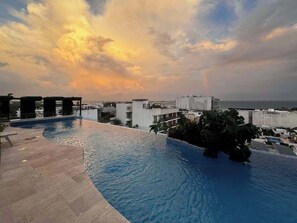 A rooftop infinity pool with a view of the ocean and buildings. - Chic Studio · Rooftop Pool · 1 Blk to 5th Ave (Playa del Carmen)