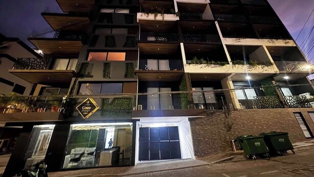 A multi-story building with balconies, a ground-level entrance, and a visible storefront. - Chic Studio · Rooftop Pool · 1 Blk to 5th Ave (Playa del Carmen)