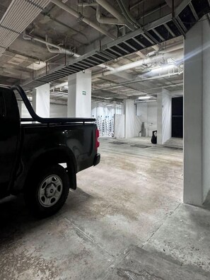 Eine Parkgarage mit Betonböden und weißen Säulen, ein schwarzer Pritschenwagen steht geparkt und eine Person befindet sich in der Ferne.