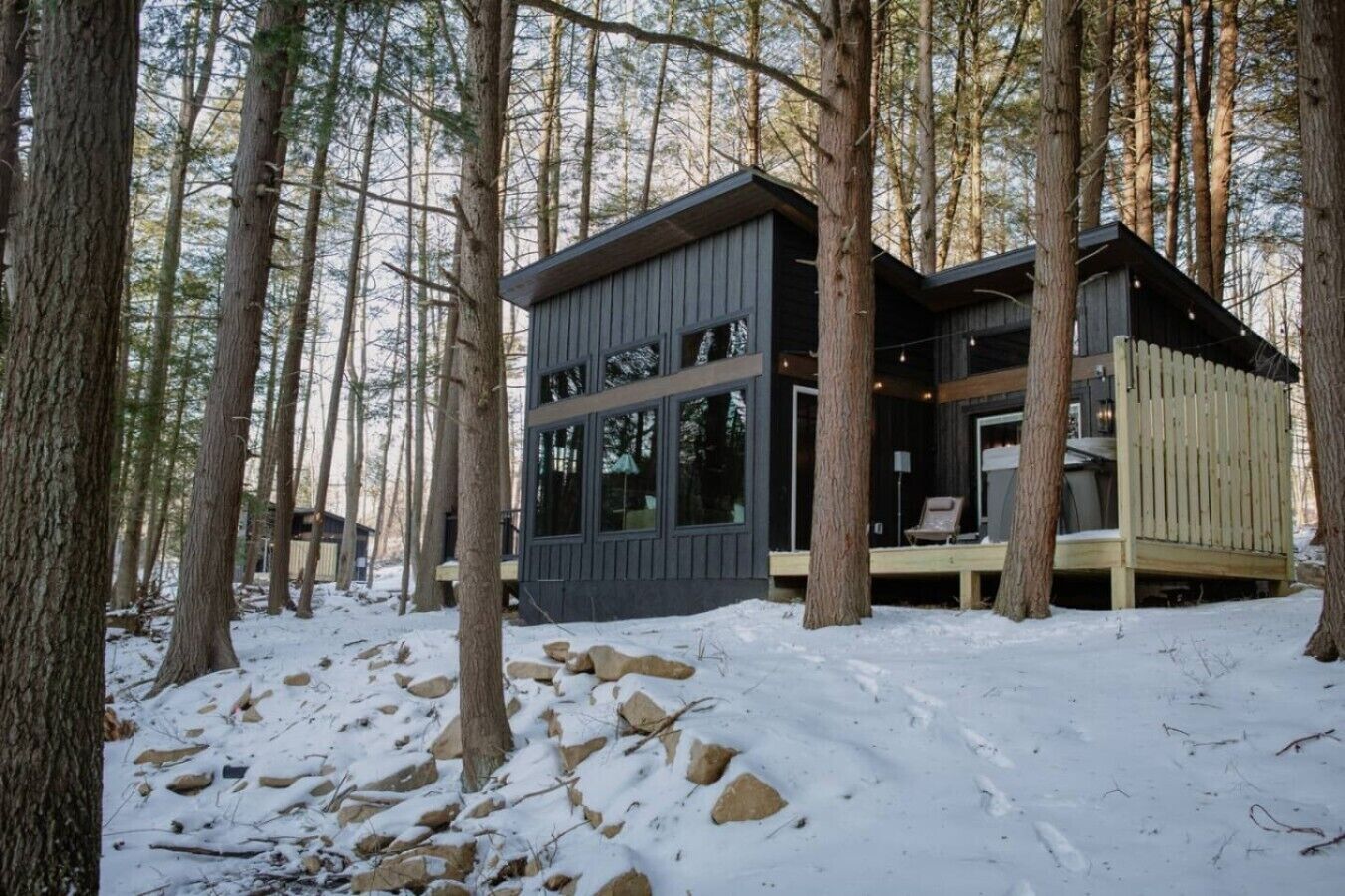 A cabin with a deck, surrounded by trees and snow.