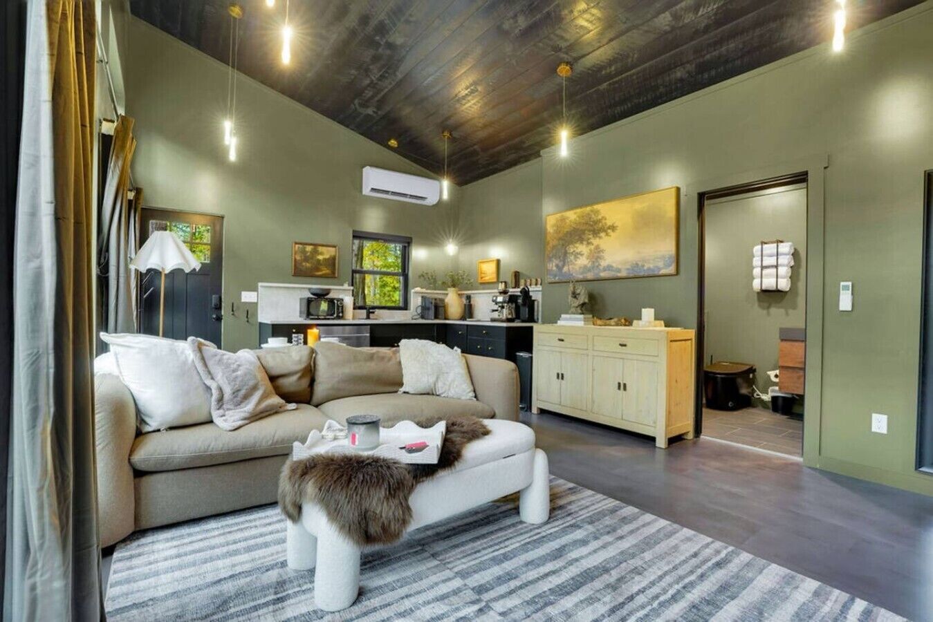 A modern living room with a sofa, a coffee table, and a fireplace. There is a kitchen area with a microwave and a sink.