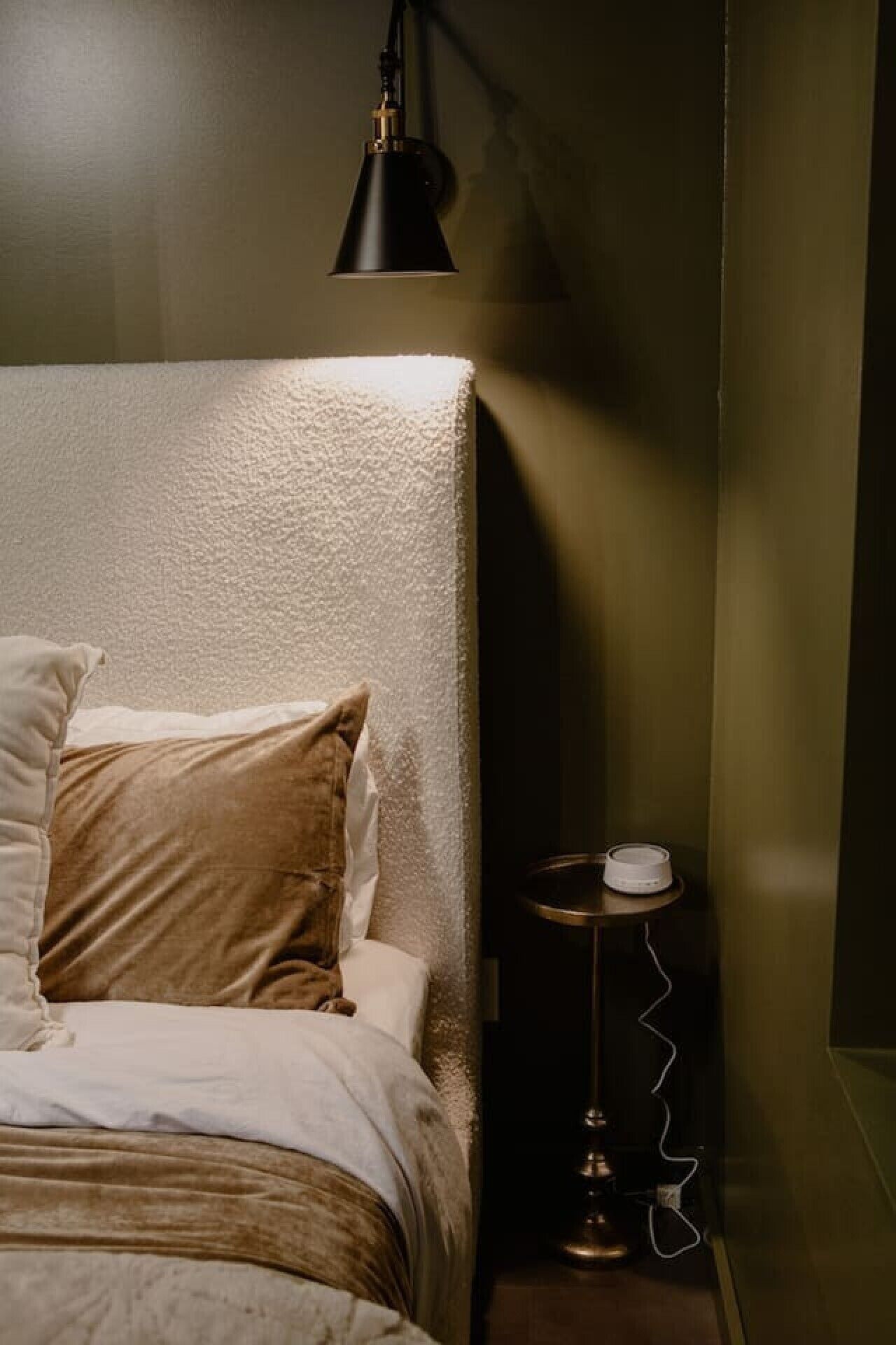 Ein Schlafzimmer mit einem Bett, Kissen, einem Nachttisch mit Lampe und einer Wandleuchte.