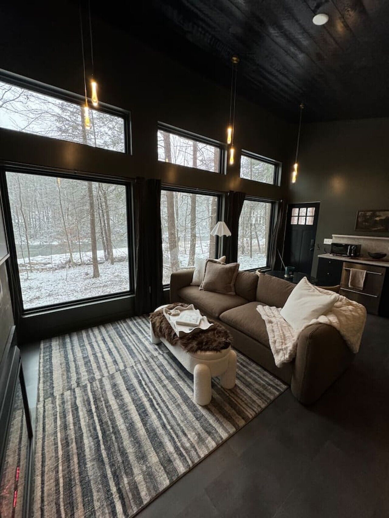 A modern living room with a large window, a sofa, a coffee table, and a lamp.
