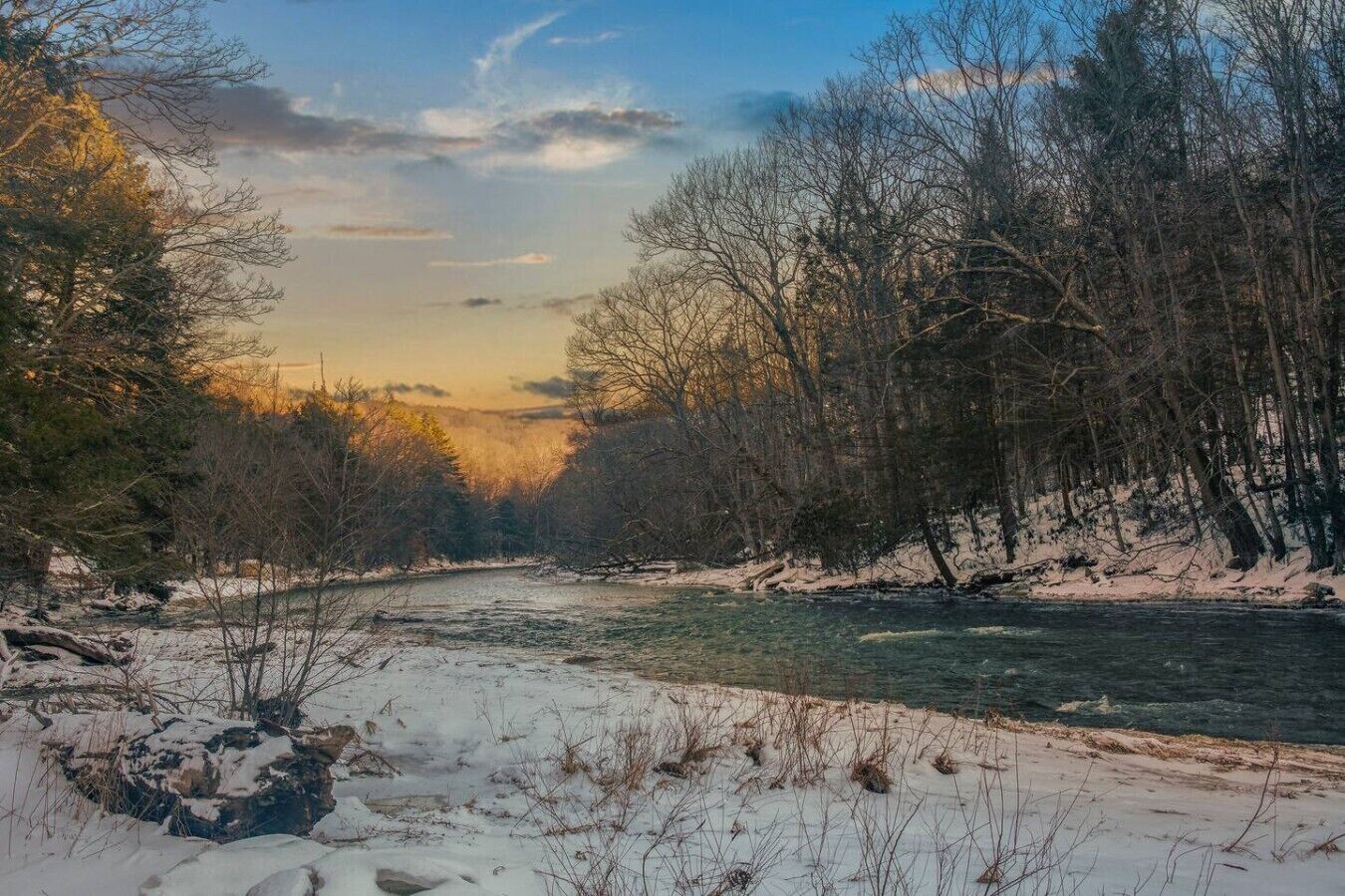 A river flowing through a forested area with snow on the ground.