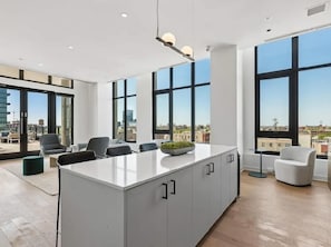 Ein moderner Arbeitsraum mit einem großen Insel-Schreibtisch, mehreren Stühlen und großen Fenstern mit Blick auf die Stadt.