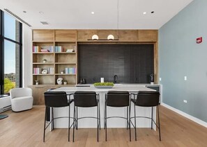 Eine moderne Küche mit einer zentralen Kochinsel, Barhocker, einem Bücherregal und einem großen Fenster.