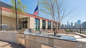 An outdoor kitchen area with a grill, a flag, and a city skyline in the background. - Luxury Penthouse Collection PH2 - Fulton Market (Chicago)