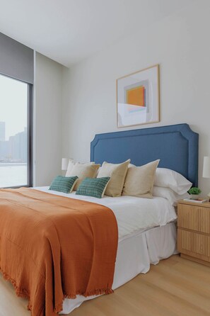 Ein modernes Schlafzimmer mit einem großen Bett, Blick auf die Stadt und einem gerahmten Kunstwerk an der Wand.