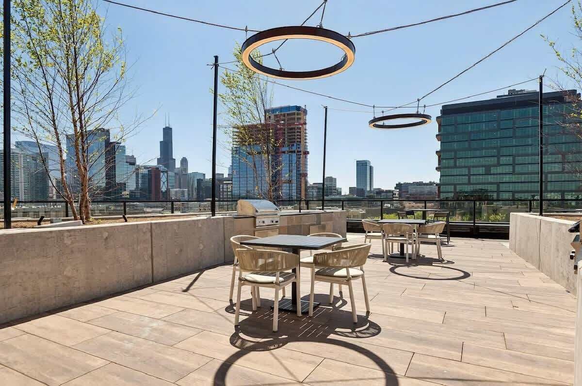 Un patio al aire libre con una mesa, sillas, una parrilla y vistas a un horizonte urbano.