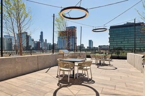 An outdoor patio with a table and chairs, a grill, and a view of a city skyline. - Luxury Penthouse Collection PH3 - Fulton Market (Chicago)