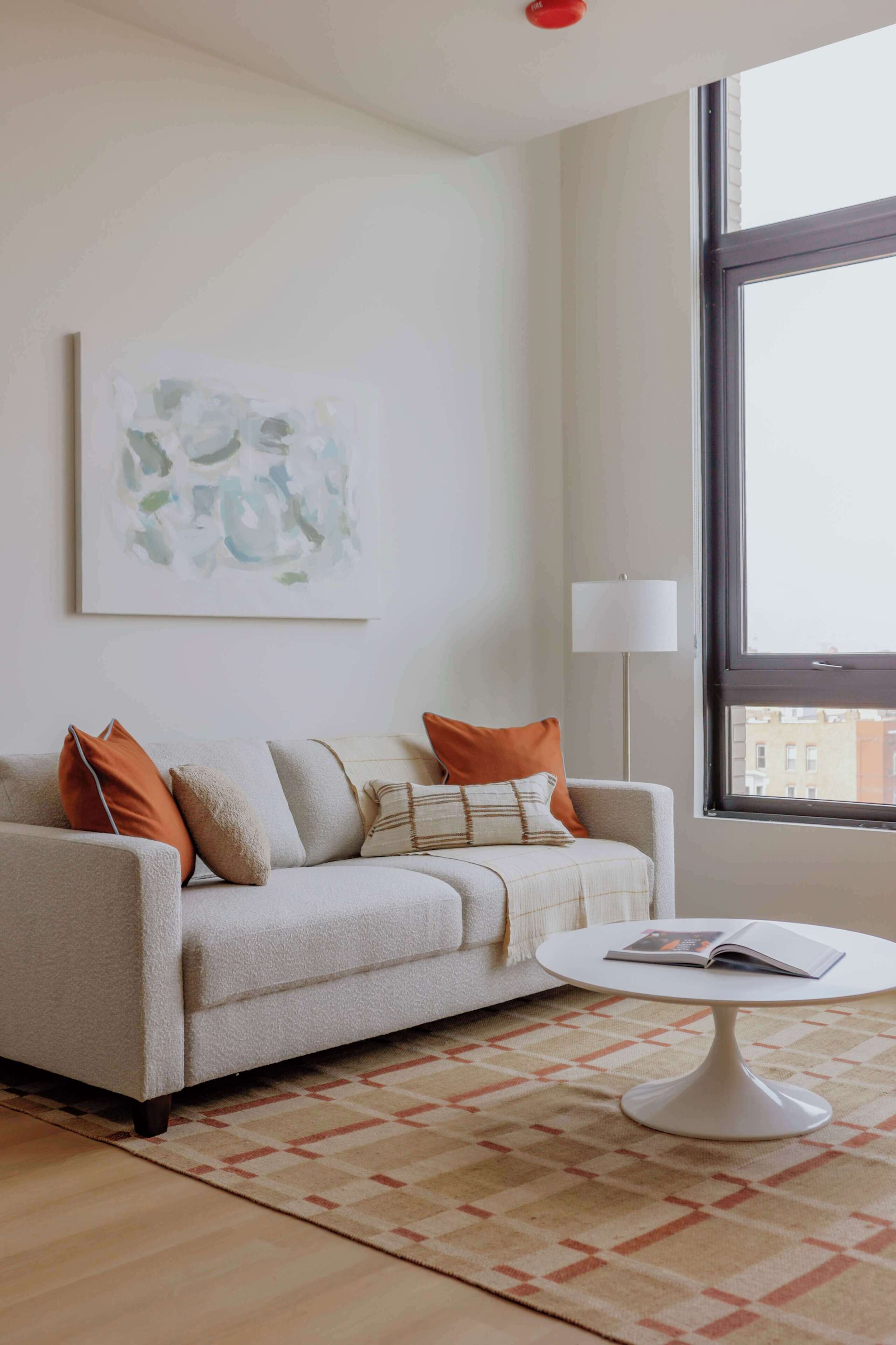 A modern living room with a sofa, a coffee table, a lamp, and a large window.