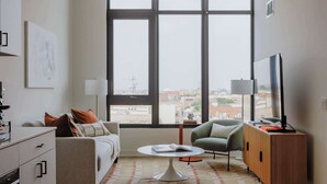 A modern living room with a sofa, armchair, coffee table, TV, and a view of the city through large windows. - Luxury Penthouse Collection PH3 - Fulton Market (Chicago)