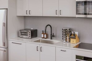 A modern kitchen with white cabinets, a stainless steel sink, a built-in oven, and a knife block. - Luxury Penthouse Collection PH4 - Fulton Market (Chicago)