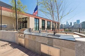 An outdoor kitchen area with a grill, a flag, and a city skyline in the background. - Luxury Penthouse Collection PH4 - Fulton Market (Chicago)