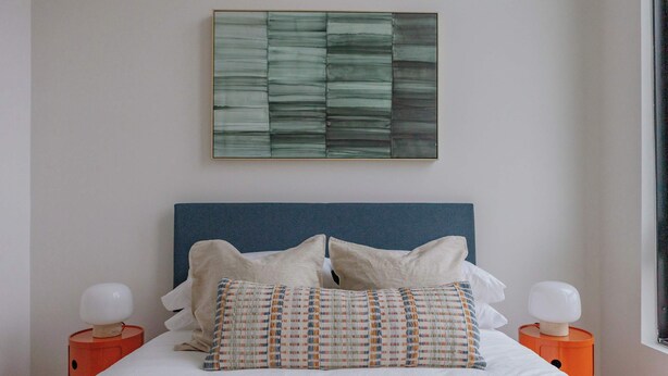A bed with a blue headboard, two white pillows, and a patterned pillow. There are two orange bedside tables with white lamps. - Luxury Penthouse Collection PH4 - Fulton Market (Chicago)