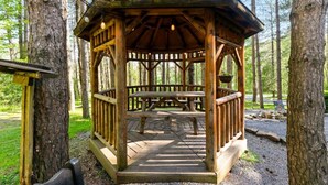 Un porxo de fusta amb taula de picnic, envoltat d'arbres.