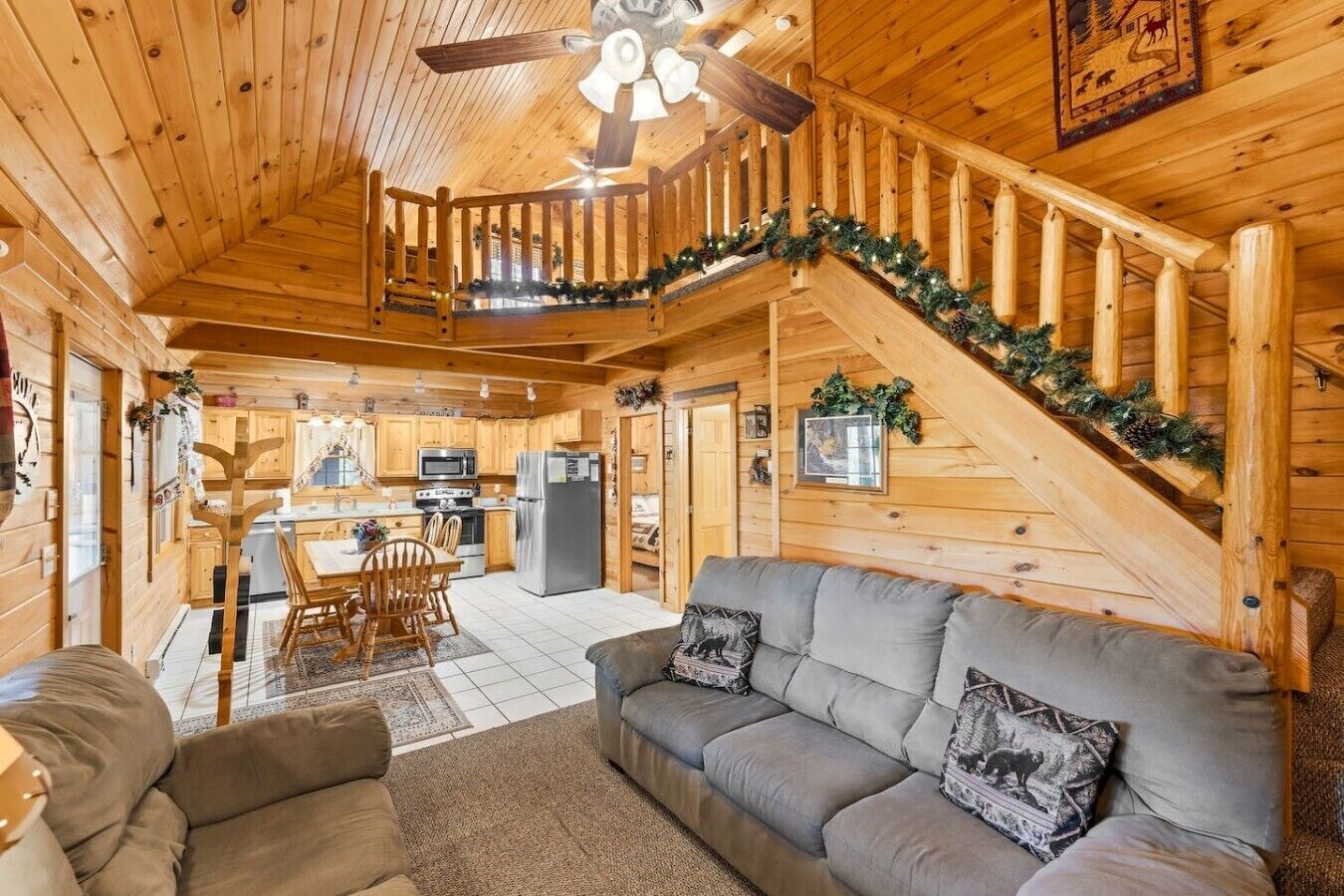 A wooden cabin interior with a dining area, kitchen, and a staircase leading to an upper level.