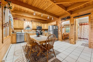 A wooden cabin interior with a kitchen, dining area, and a visible door leading outside.
